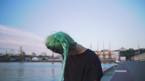 Young Stylish Funky Girl with Green Hair Dancing Near Sea Port During Sunset Getting Crazy and