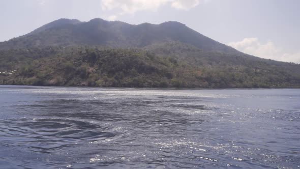 From the boat you see upswelling and current on the surface of the water. in the background a volcan