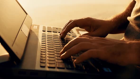 Close-up young man working on laptop outdoors. Beautiful summer sunset by the river