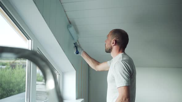 A Man Paints a Wall with a Roller