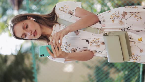 Pretty Caucasian Brown Hair Girl Wearing White Flower Dress with Bag Cross Her Shoulder Using