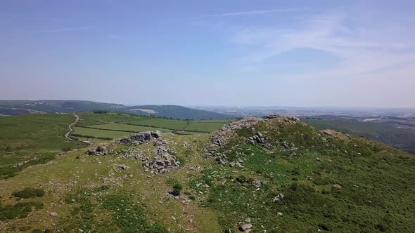 Wide shot aerial tracking forward upwards above Sharps Tor to reveal a wide expanse of countryside,