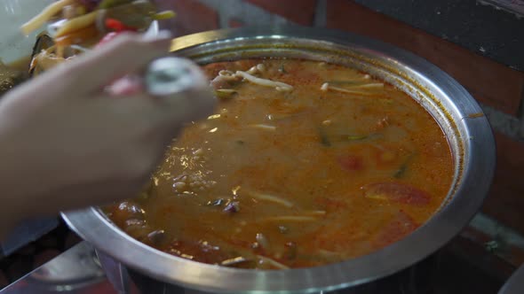 A close up shot of a girl's hand taking cooked vegetable and soup in buffet. Thai Tom Yum Soup