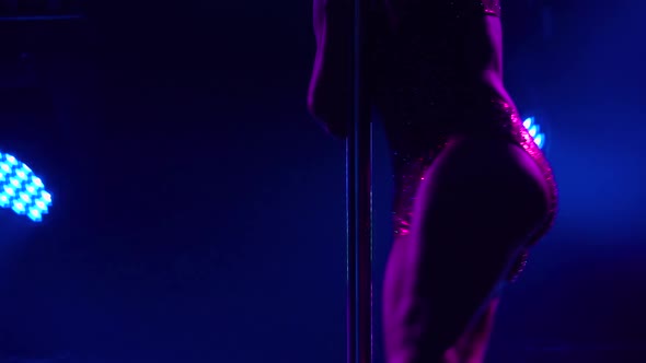 The Dancer Spins Around the Pole Upside Down in a Dark Studio