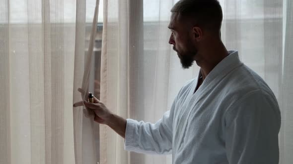 a Man in a White Coat Stands at the Window Looks at the Clock Peeks Through the Curtain and Smokes