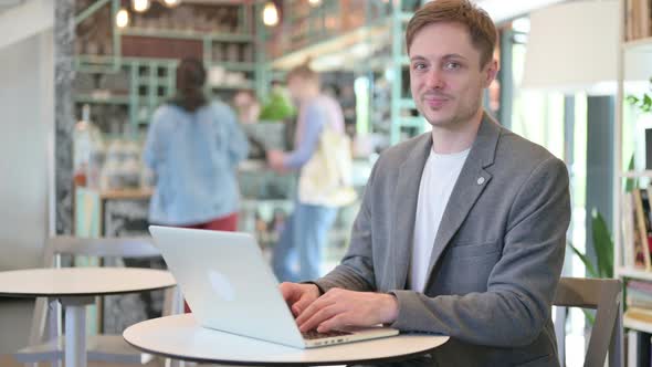 Thumbs Up By Young Man with Laptop in Cafe