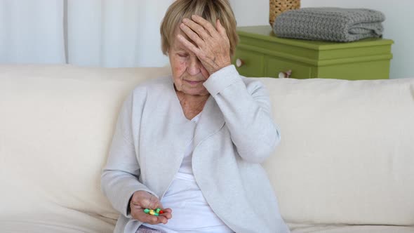 Sick Old Woman With Headache Holding Pills At Home.