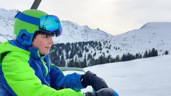 Handsome Boy with Ski Going Up on Chairlift in Mountains