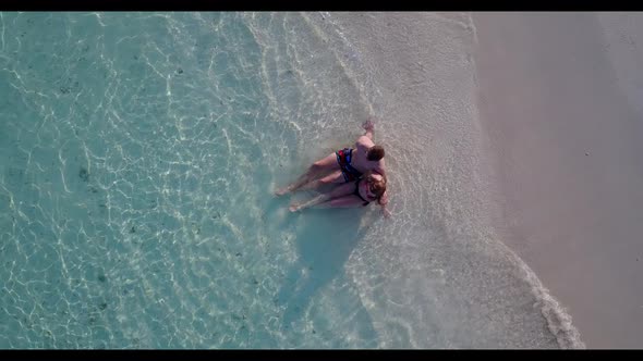 Teenage lovers tanning on idyllic coastline beach adventure by blue green sea and white sand backgro