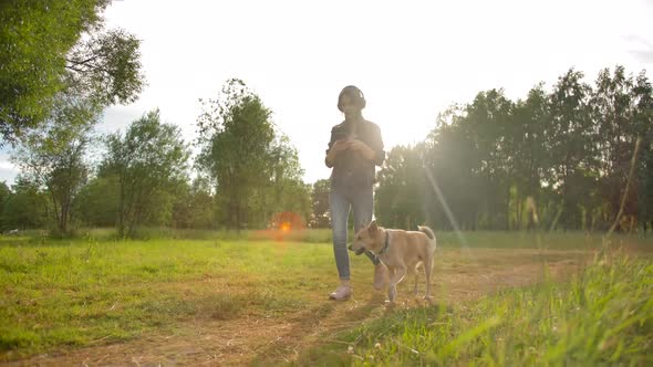 A Girl in Headphones Walks with Her Dog in the Park. Front Wide Slow Motion View.