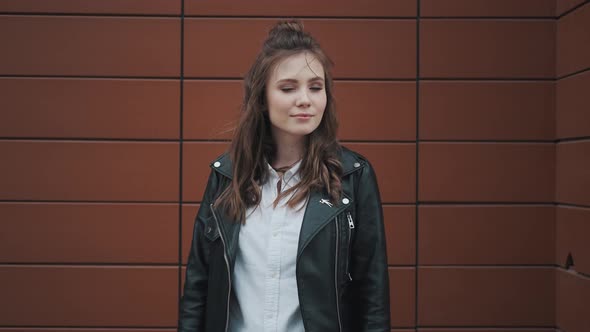 Hipster Girl in a Leather Jacket on the Background of Modern Architecture. Girl Looks and Smiles at
