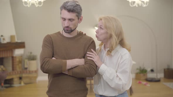 Senior Blond Caucasian Woman Calming Down Bearded Man with Gray Hair at Home. Sad Adult Son Sharing