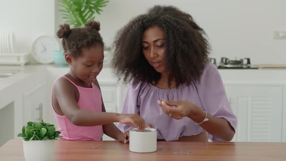 Delightful Young Loving Mother Helping Her Adorable Little Daughter in Saving Money By Collecting