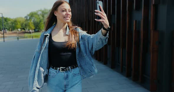 Portrait of Young Beautiful Woman Blogger in City Holds Phone Taking on Mobile Camera Shoots Video