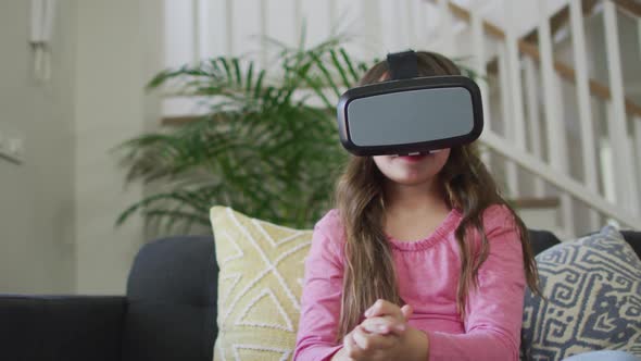 Caucasian girl wearing vr headset, sitting on sofa and having fun