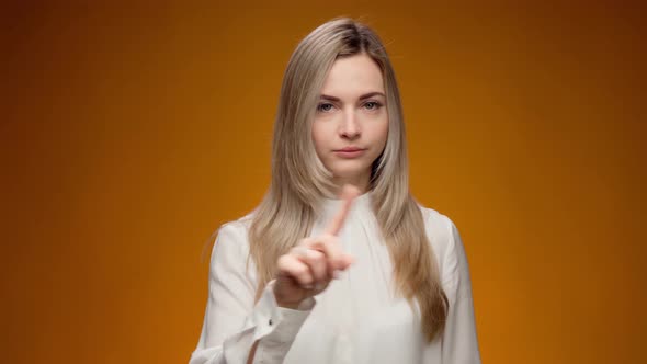 Young Woman Wags a Finger Rejecting Something Against Yellow Background