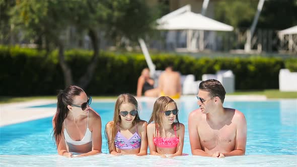 Happy Family of Four in Outdoors Swimming Pool