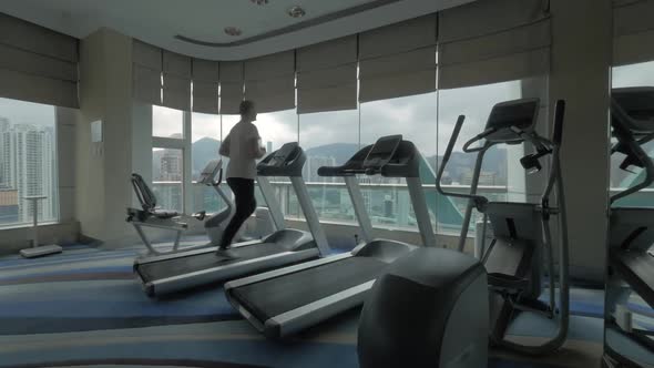 Clip of woman on the treadmill in fitness centre looking at window with cityscape Hong Kong, China