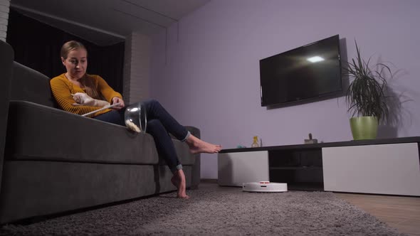 Robot Cleaner Working While Woman Relaxing on Sofa