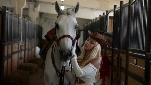 Sexy Lady is Holding Reins of Beautiful White Horse in Stable