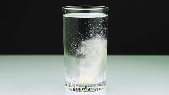 An Effervescent Yellow Tablet Against Pain Falls Into a Glass and Dissolves Slow-motion Shot of