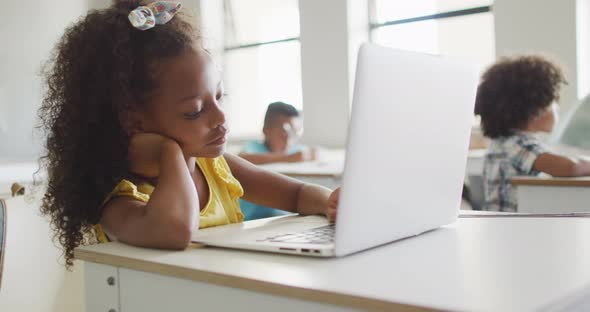 Video of bored african american girl sitting at desk with laptop during lesson in classroom