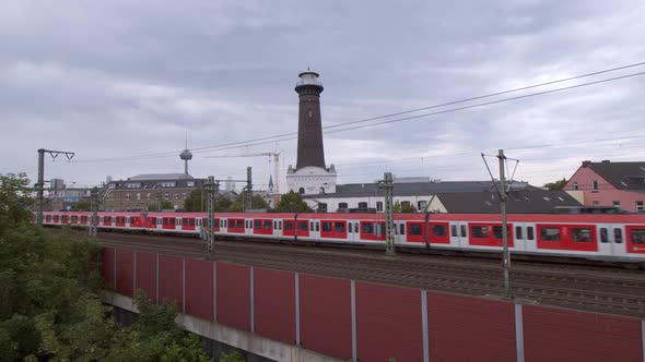 Cologne Ehrenfeld, Germany 2022 - Red commuter train passes with tower in the background on a cloudy