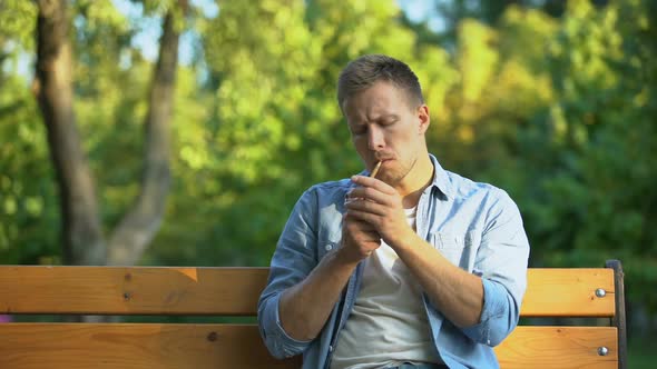 Pensive Young Man Smoking Cigarette, Relaxing on Bench at Park, Harmful Habit