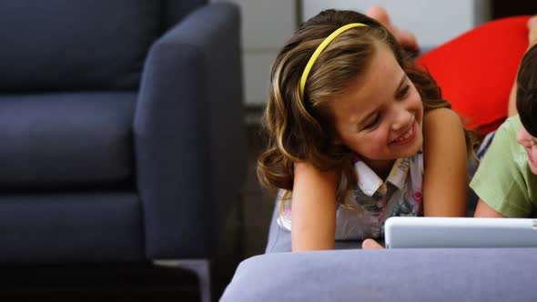 Siblings using digital tablet in living room alt