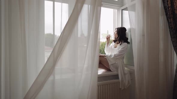 Bride in Boudoir Dress Sitting on Window Sill Wedding Morning Preparations Woman in Night Gown Veil