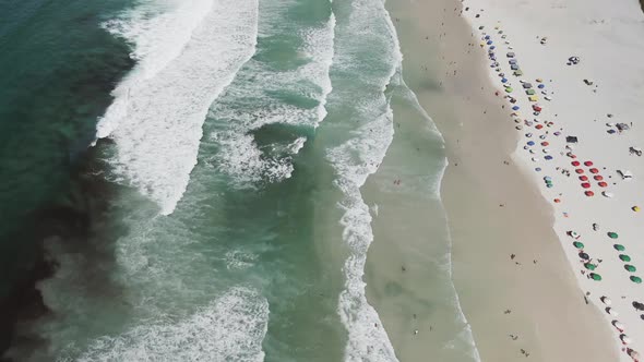 Waves rolling into white sand beach full of tourist in Rio de Janeiro, Brazil