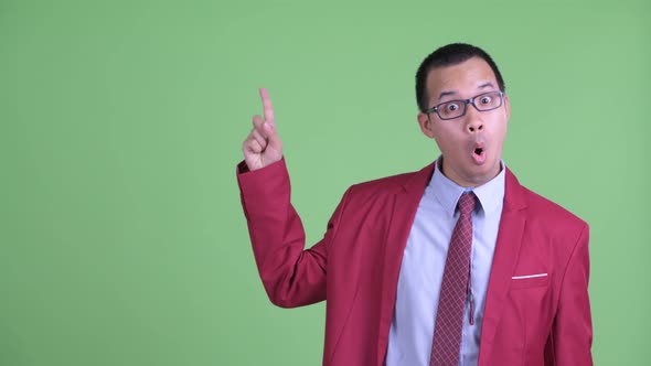 Happy Asian Businessman with Eyeglasses Pointing Up and Looking Surprised