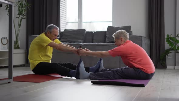 Active Mature Couple Performing Stretching Exercise Together on the Yoga Mat