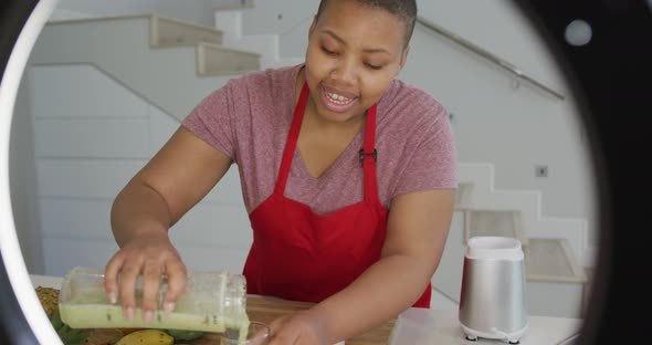 Happy african american plus size woman wearing apron, making cooking vlog with camera in kitchen