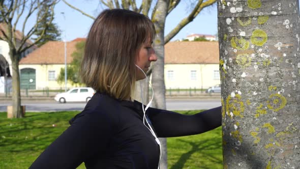 Sporty Young Woman in Earphones Exercising in Park