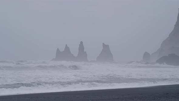 Static, shot, of waves hitting a black sand beach and cliff, on the arctic sea, on a cloudy, stormy