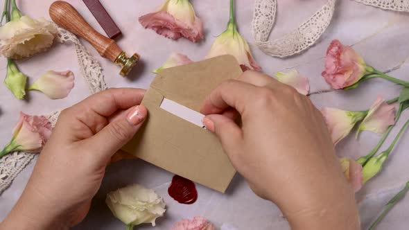Hands opening an envelope with a MARRY ME card near pink flowers