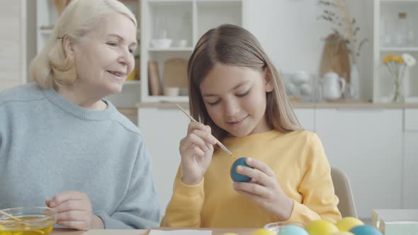 Cute Girl Drawing on Easter Egg with Help of Grandma