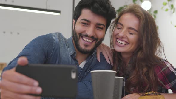 Happy couple with phone making video call in cafe
