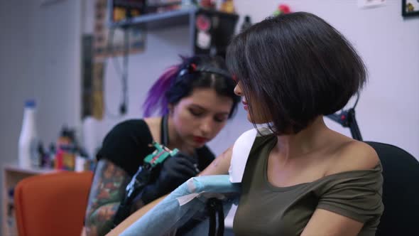 A Closeup View of a Professional Woman Tattooist Who is Tattooing on the Leg of a Young Girl