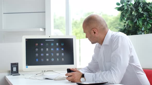 Office Worker is Sitting at a Personal Computer He Looks at the Camera