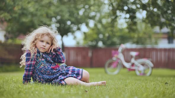A Little Girl in the Garden on the Grass with Her Bicycle in the Background