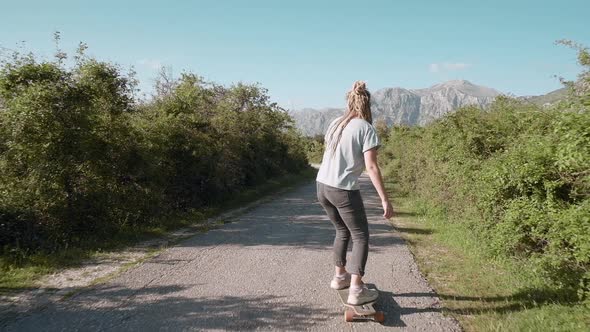 Back view of dreadlocks woman longboarding on mountain background riding skateboard on road
