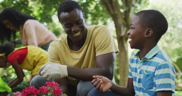 Animation of happy african american father and son planting flowers in garden