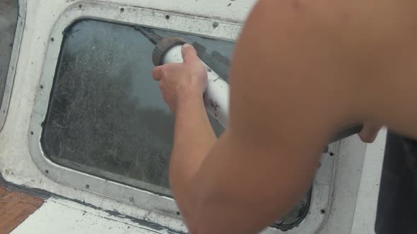 Applying sika flex mastic sealant on bow windows of wooden boat using sealant gun.