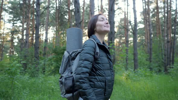Young Woman in a Jacket with a Backpack Enjoys the Atmosphere of Coniferous Forest