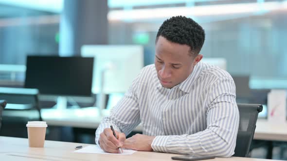 Pensive African Businessman Writing on Paper Thinking