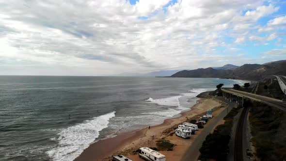 Aerial drone shot rising high over a cloudy beach in Ventura with surfers in the Pacific Ocean and R