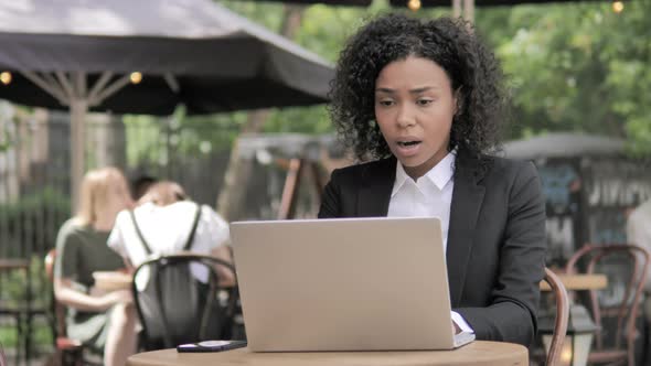 African Businesswoman in Shock by Results on Laptop in Outdoor Cafe