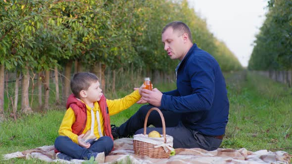 Family Picnic Male Child Takes Juice From His Fathers Hands and Pours It Into Clear Glass